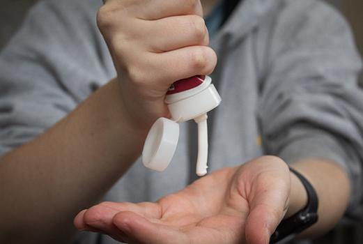 Hand dispensing white lotion from a pump onto an open palm