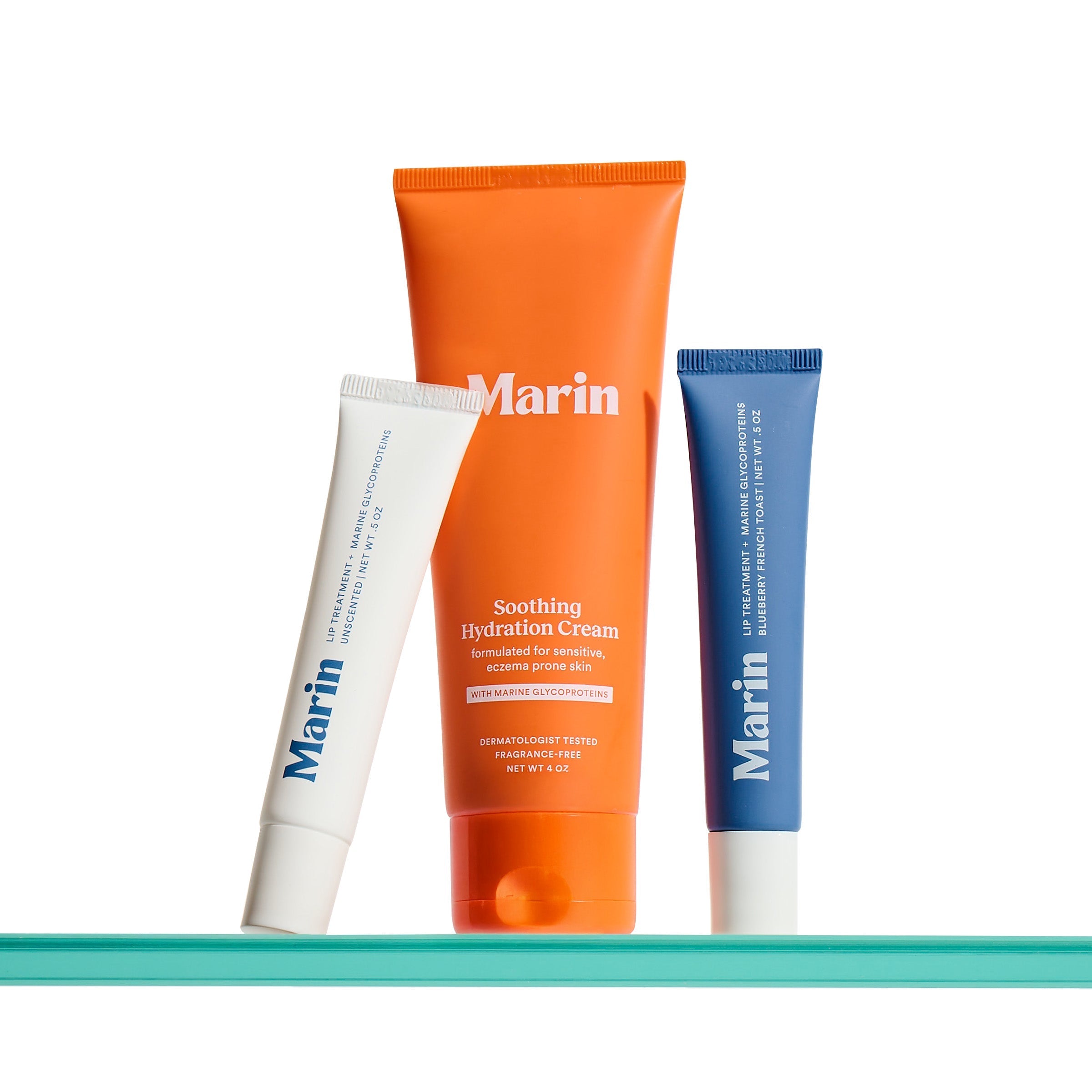 Three Marin product tubes on a glass shelf — orange tube labeled Marin Soothing Hydration Cream, flanked by white and blue Marin tubes