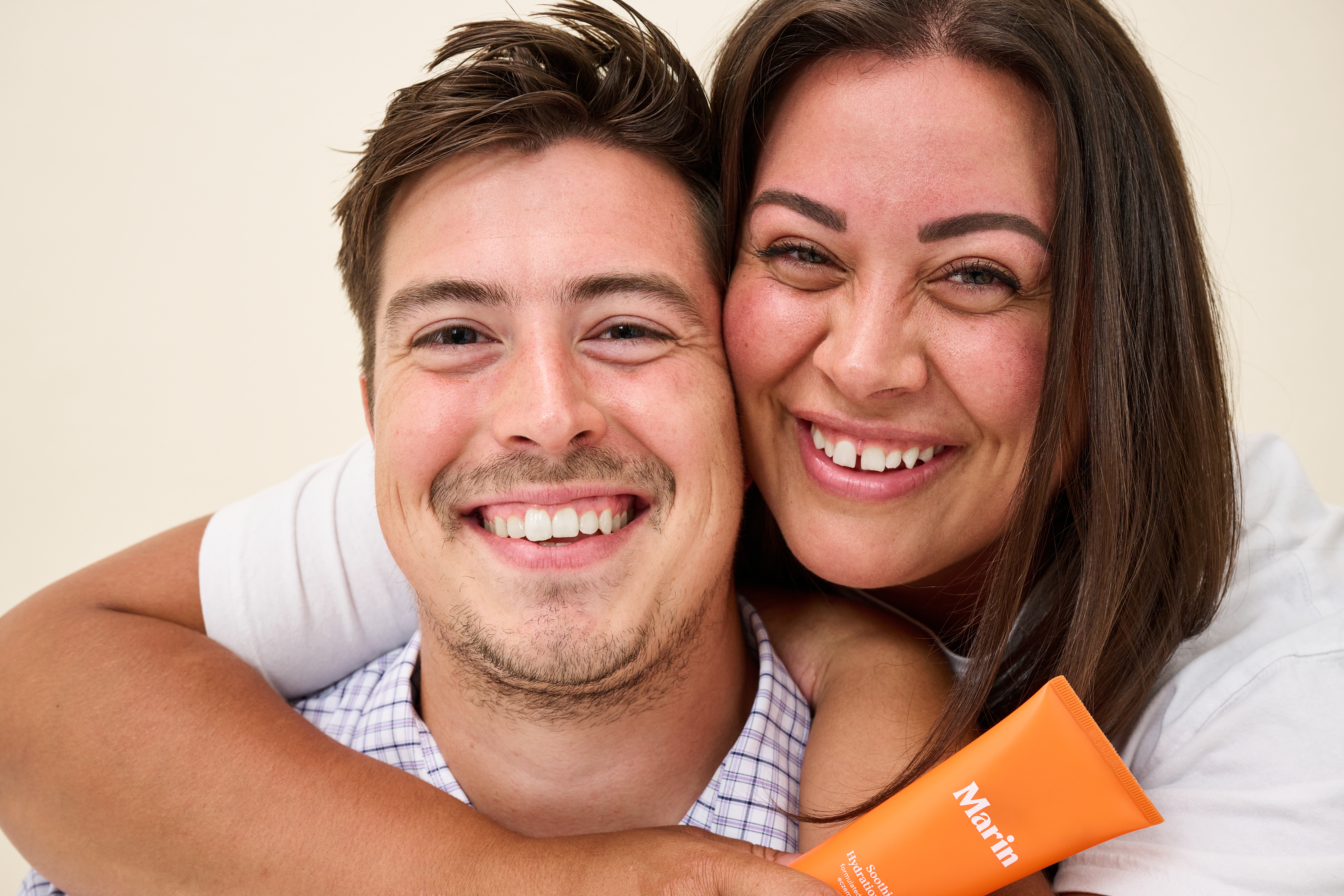 Smiling man and woman hugging, woman holds orange Marin skincare tube in foreground