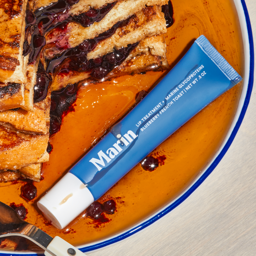 Marin blue lip treatment tube, 'Blueberry French Toast' flavor, on syrupy plate beside French toast and blueberries