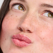 Young woman with freckles and hazel eyes puckering her lips, looking up and to the right