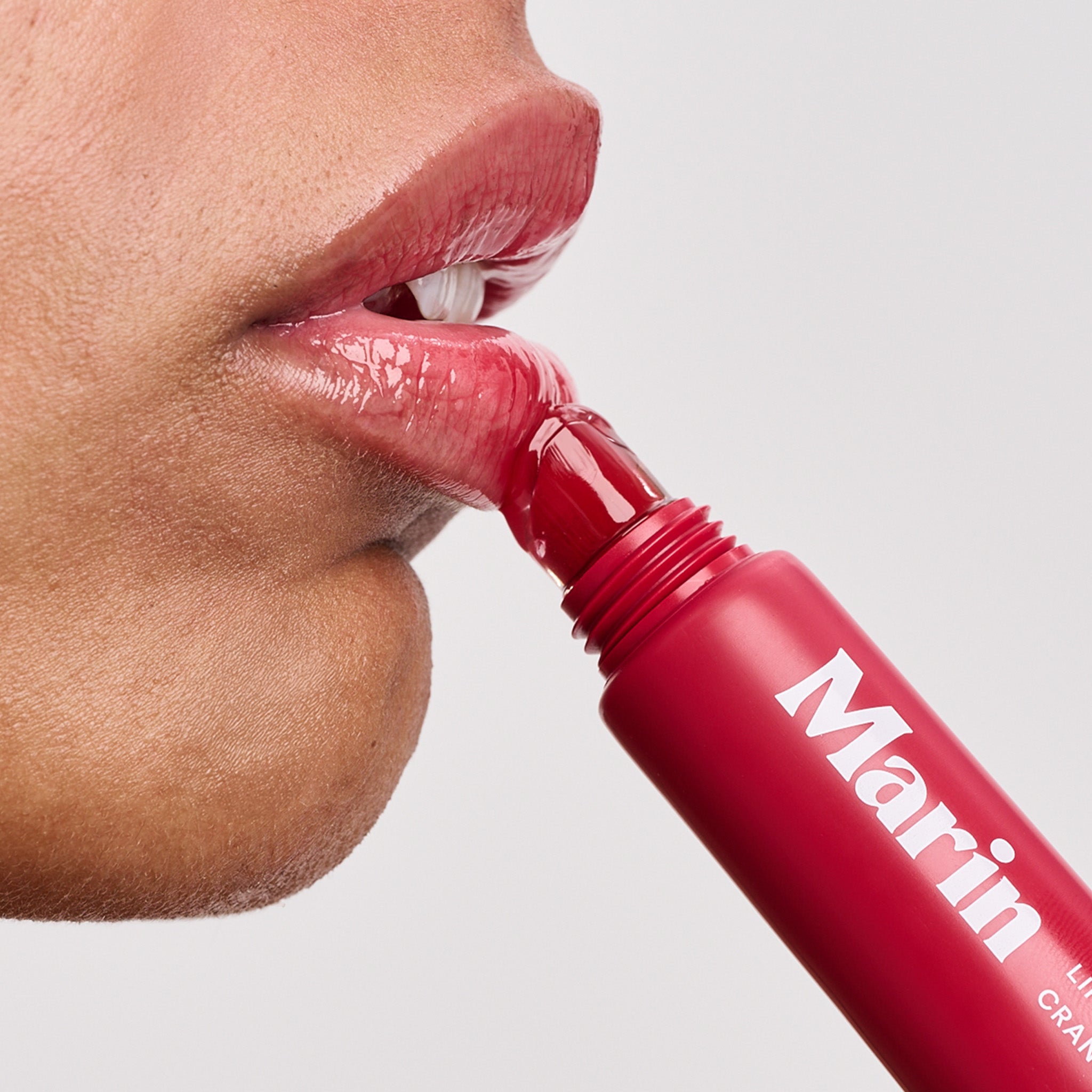 Person applying red lip gloss with 'Marin' printed on the tube
