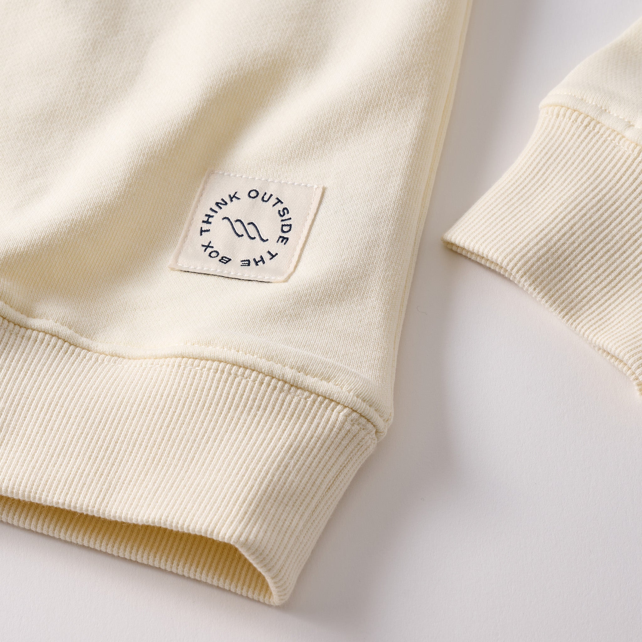 Cream sweatshirt cuff and hem with stitched square patch reading THINK OUTSIDE THE BOX