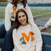 Smiling woman on a field bench wearing sweatshirt with large orange M and patches reading MARIN and go Blue