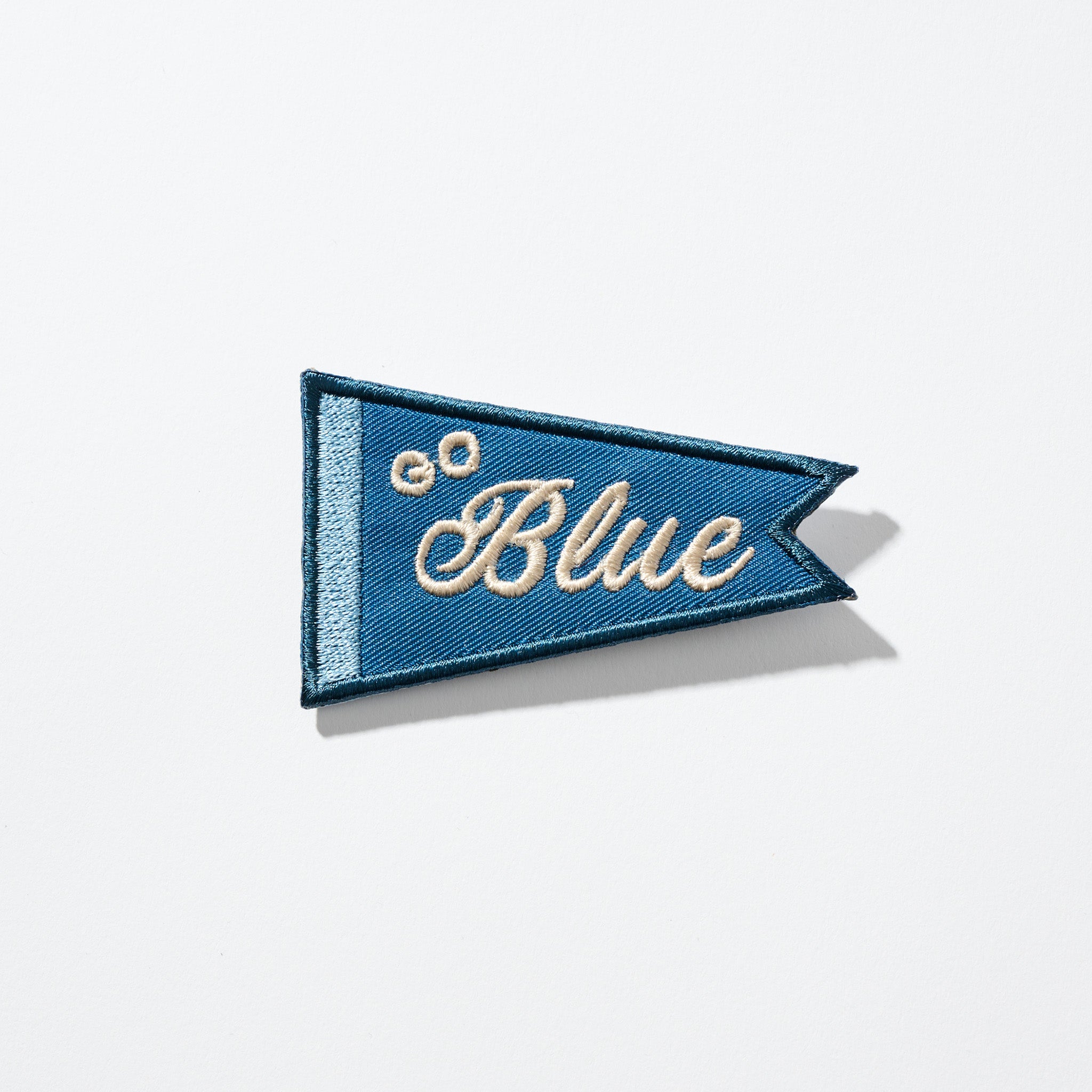 Blue triangular embroidered pennant patch with cream script 'Blue' and two small cream embroidered circles.