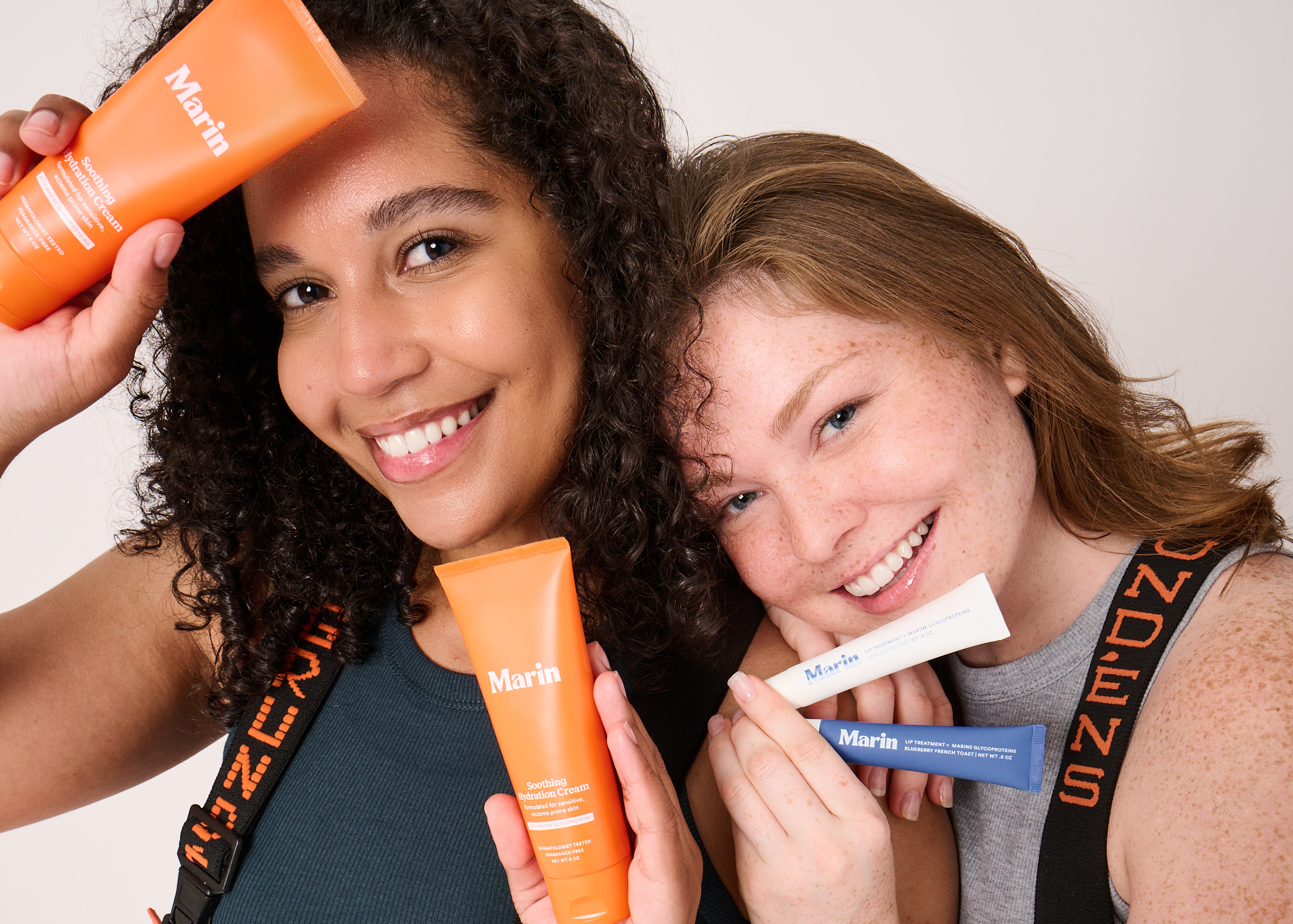 Two women holding Marin products: Marin Soothing Hydration Cream; Marin LIP TREATMENT; strap ZUZENS.