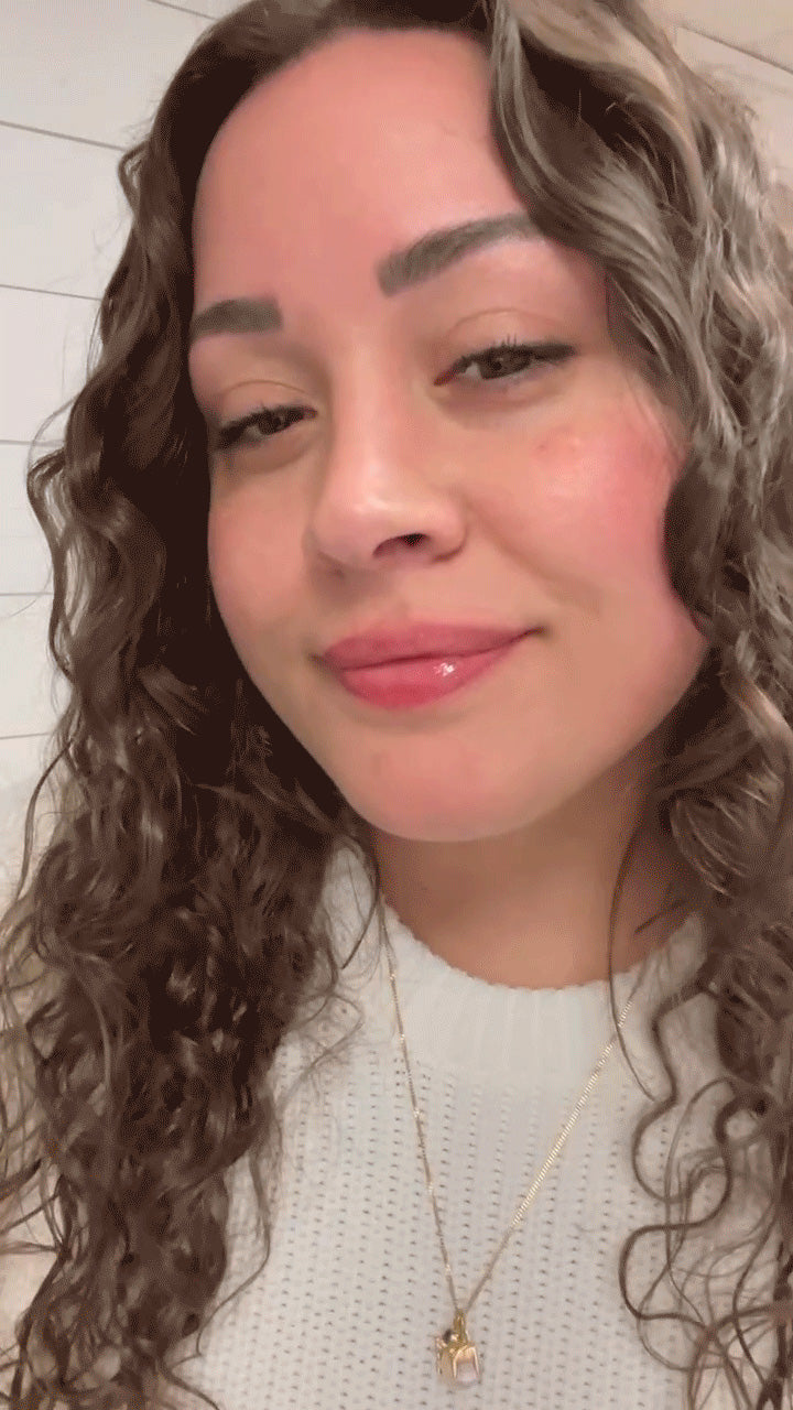 Smiling woman with dewy skin, light pink lip gloss, curly hair and gold pendant over white sweater — Marin Skincare selfie