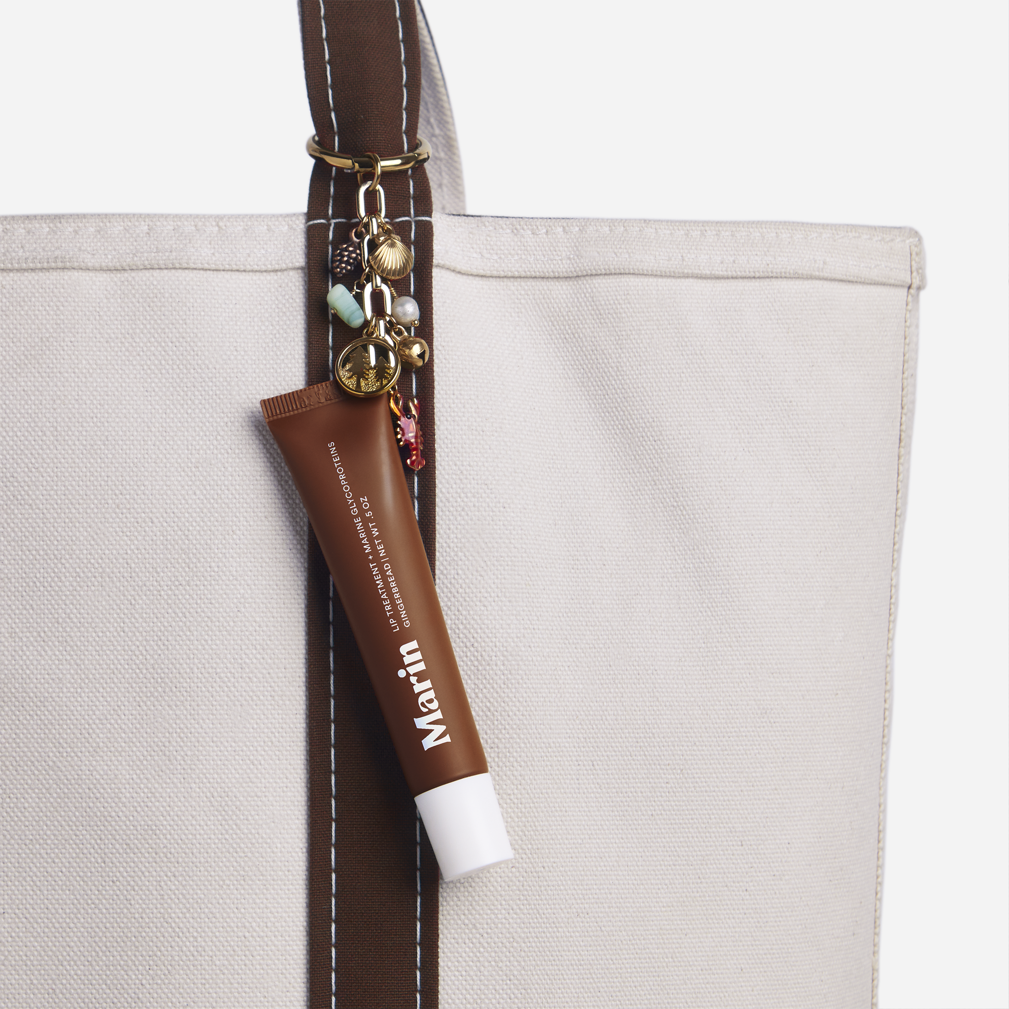 Canvas tote with brown strap and a Marin lip-tube charm hanging from the handle.