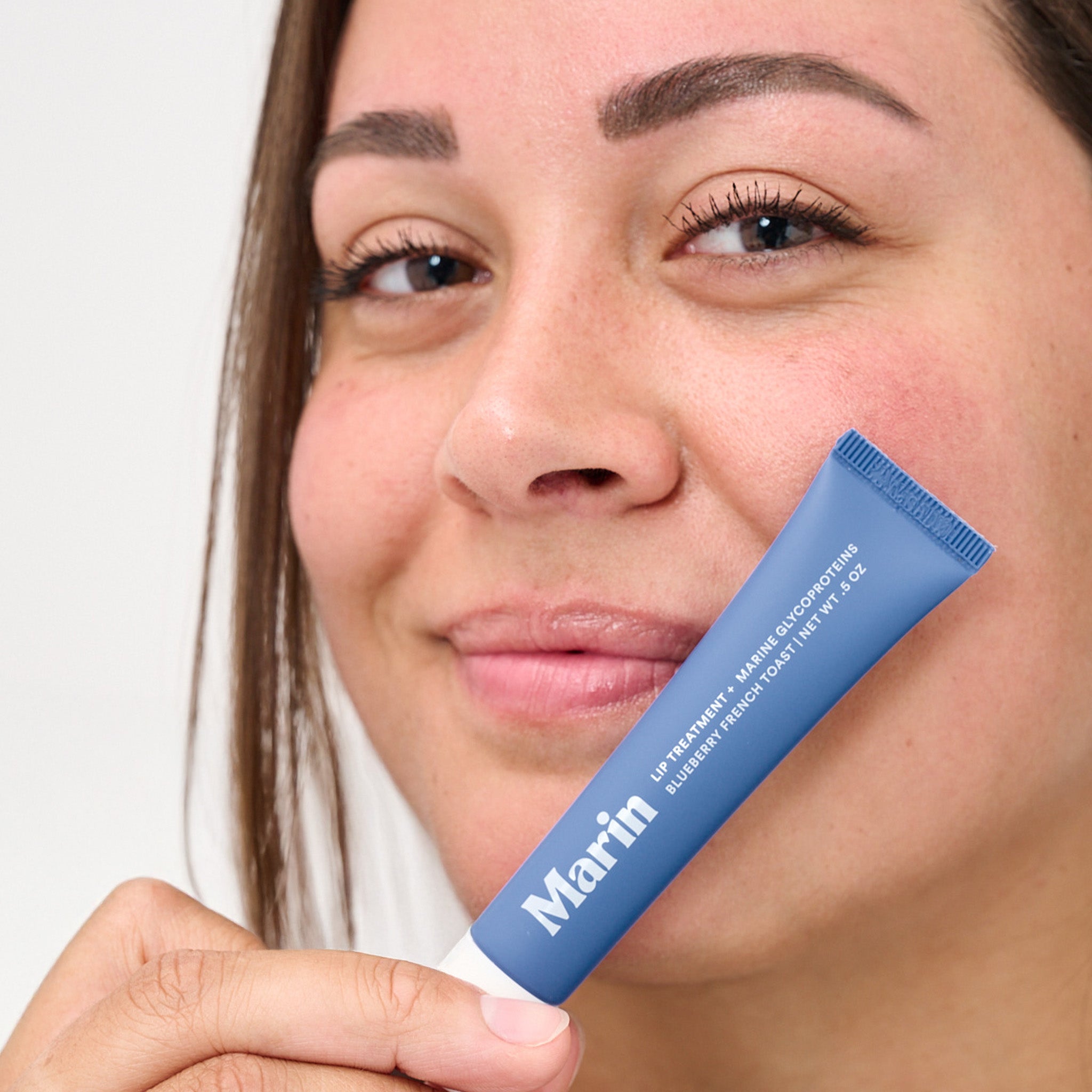 Person holding a tube labeled: Marin LIP TREATMENT + MARINE GLYCOPROTEINS BLUEBERRY FRENCH TOAST NET WT .5 OZ