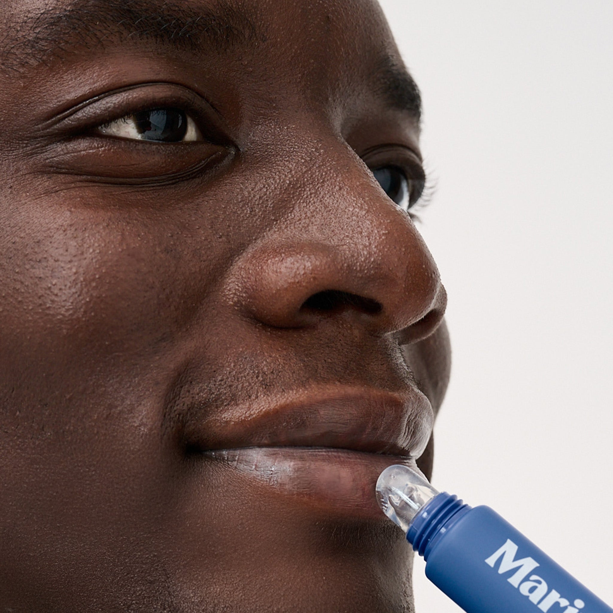 Close-up of a person applying clear lip treatment from a blue tube labeled Marin on lower lip.