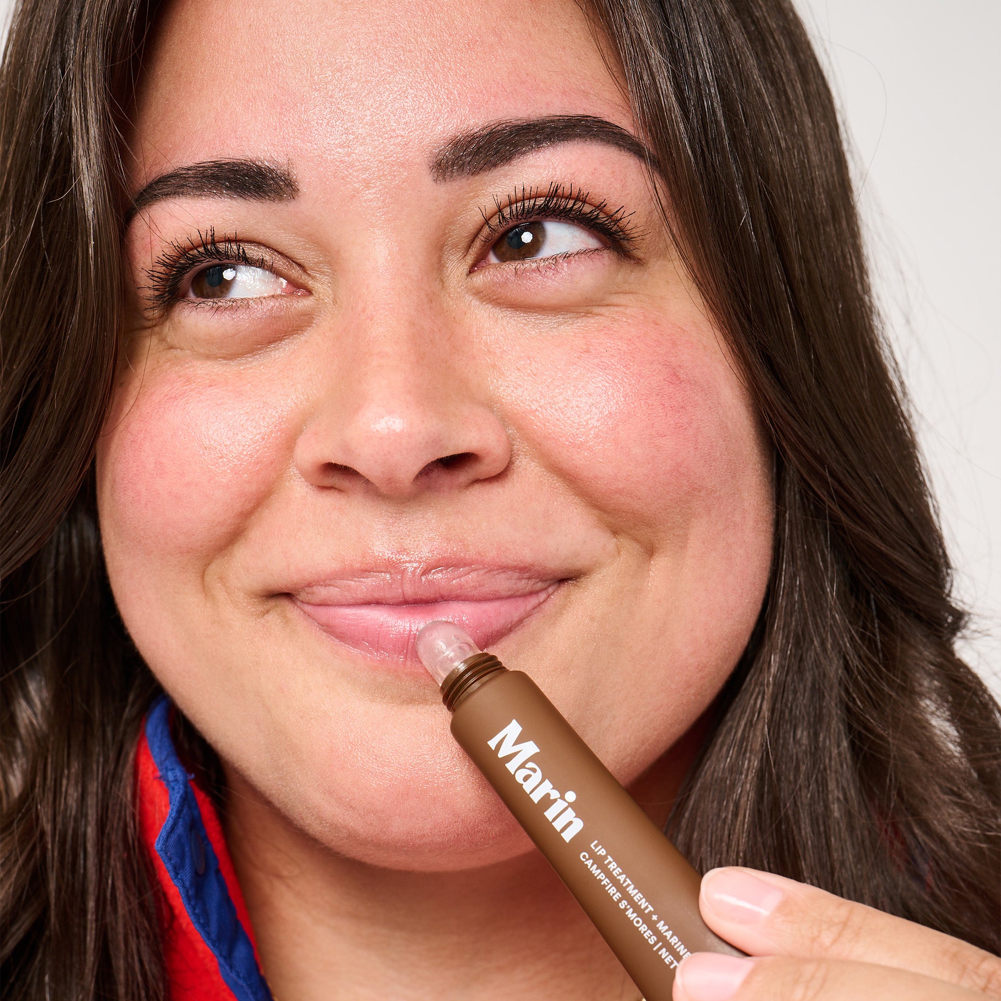 Woman applying Marin lip treatment tube labeled Marin, LIP TREATMENT, CAMPFIRE S'MORES to lower lip.