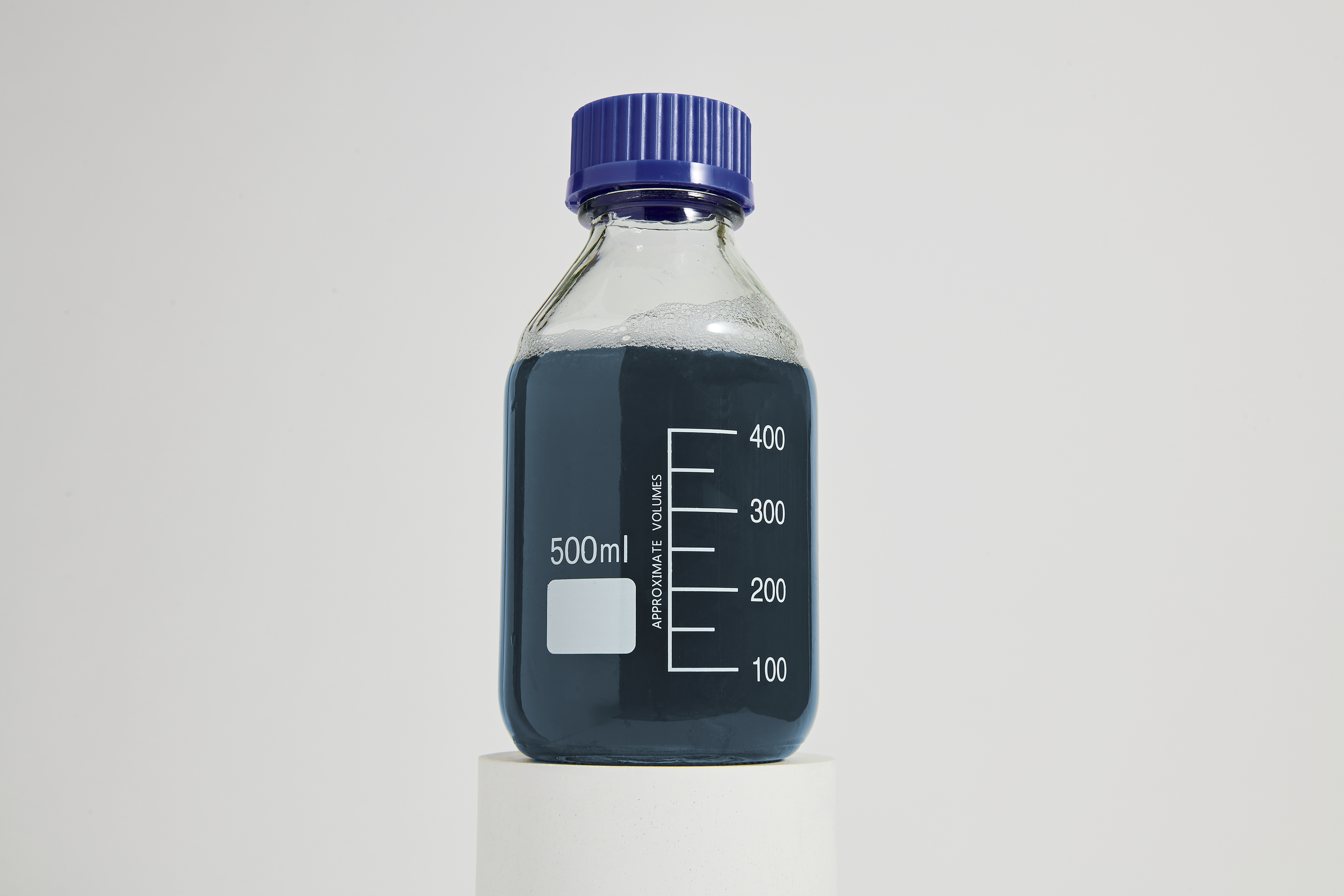 Clear lab bottle with blue liquid on a pedestal, marked '500ml', scale '100 200 300 400', 'APPROXIMATE VOLUMES'.