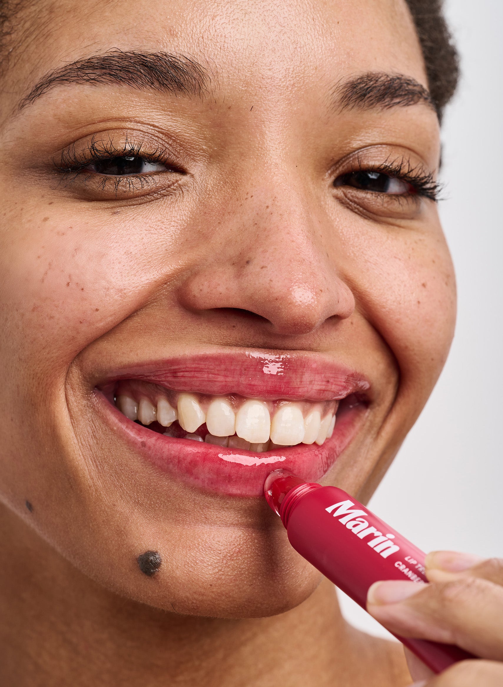 Smiling face applying Marin glossy red lip tinted treatment to lower lip