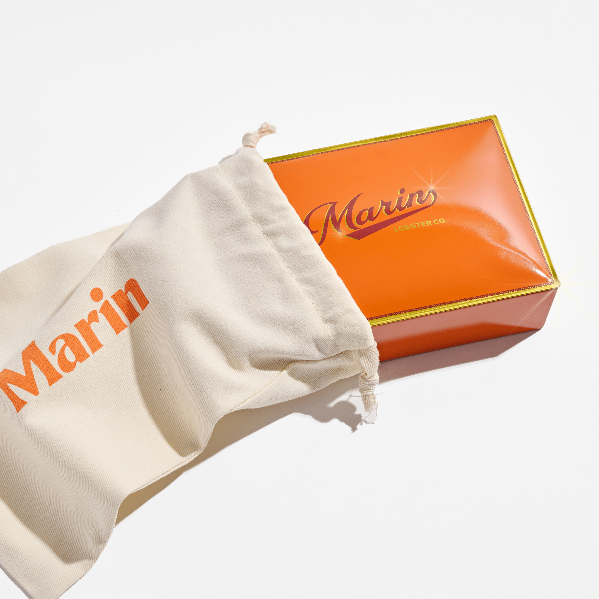 Orange box labeled Marin and LOBSTER CO., partially inside a cream drawstring bag printed with Marin.